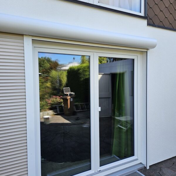 Moderne Terrassenfenster mit weißem Rahmen und integriertem Rollladensystem an einem Wohnhaus.