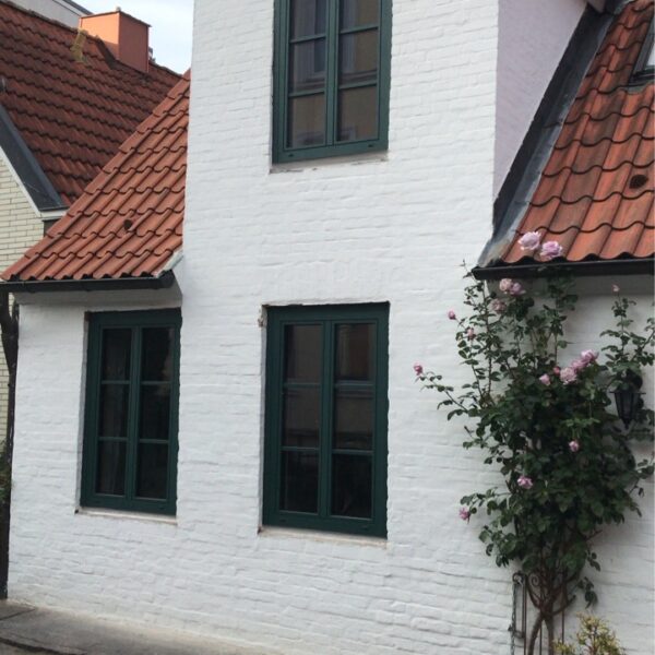 Weiße Hausfassade mit roten Dachziegeln und grünen Fenstern.