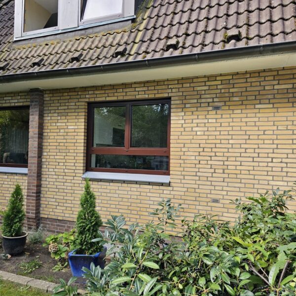 Braunes Kunststoff-Dreh-Kipp-Fenster mit festem Seitenteil in Klinkerfassade.