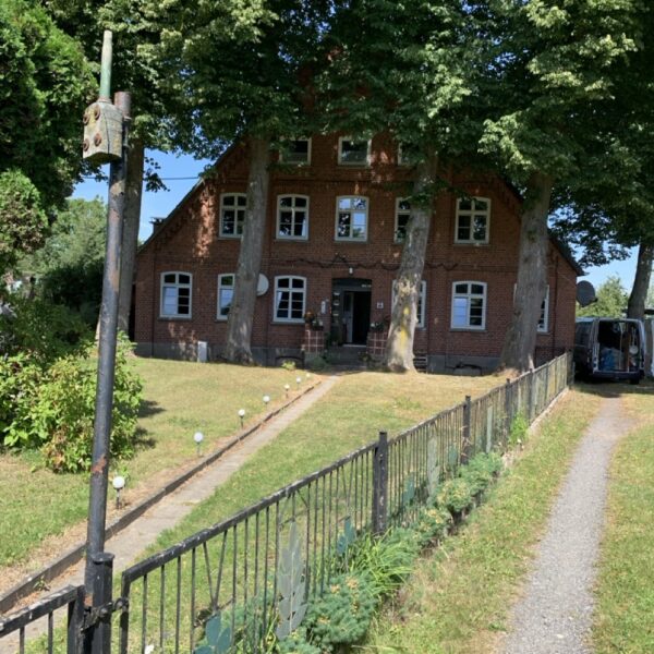 Historisches Backsteinhaus mit Vorgarten, alten Bäumen und Metallzaun.